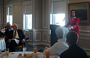 Image of a  woman wearing a red suit jacket speaking from a podium.