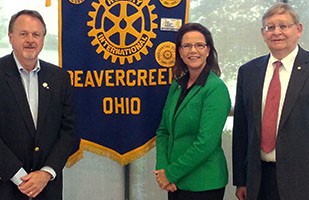 Image of a  woman wearing a green suit standing between two men, both wearing dark suits.