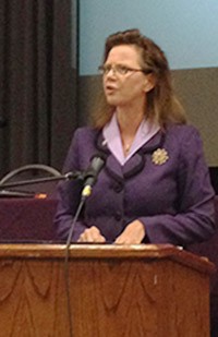 Image of a woman wearing a purple suit speaking from a podium.