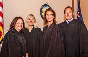 Image of three female judges and one male judge, all wearing black judicial robes.