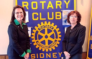 Image of a  woman wearing a a blue suit and a green blouse standing next to a woman wearing a black suit.