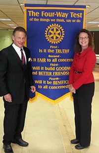 Image of a woman wearing dark dress pants and a red suit jacket standing next to a man wearing a dark suit.