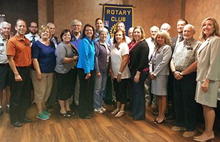 Image of a group of men and women standing in front of a blue rotary banner.