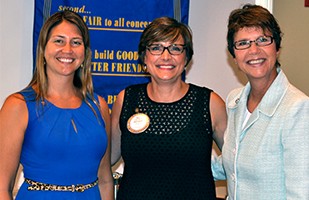 Three women standing side-by-side, one wearing a royal blue dress, one wearing a black dress, and one wearing a light blue suit.