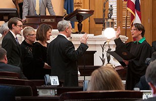 A female judge wearing a black judicial and green blouse stands in front of a small group of men and women.