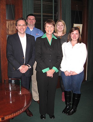 Image of a woman wearing a black suit and green blouse standing with two men and two women.