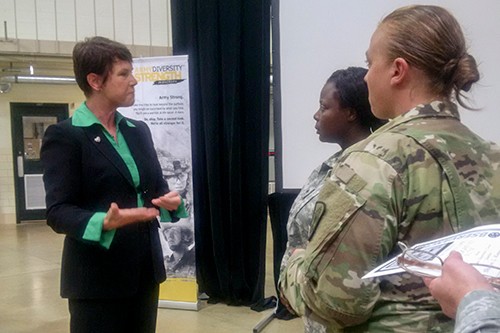 Image of a woman wearing a black suit and green blouse speaking to two women dressed in fatigues.