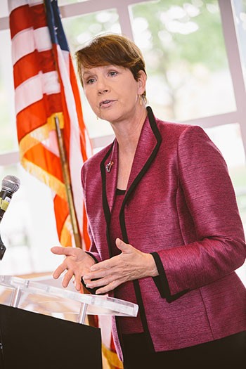 Image of a woman wearing a red and black suit speaking from a podium.