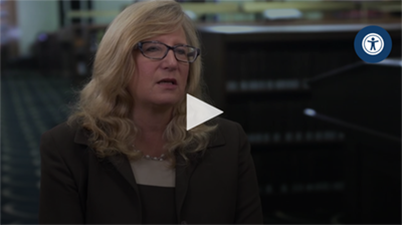 Woman with long, light brown hair wearing a suit and glasses.