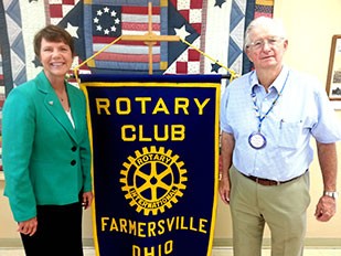 Image of a woman wearing a green suit jacket and black dress pants standing next to a man wearing khaki pants and a short-sleeve dress shirt.