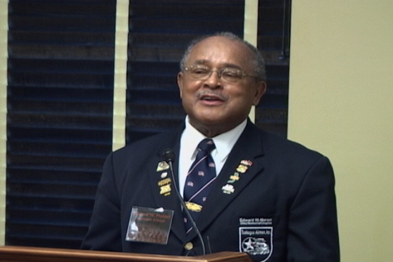 Image of an African American man wearing a blue dress military uniform speaking from behind a podium