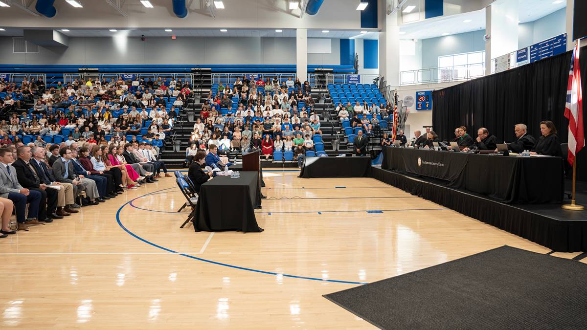 Seven justices sitting in front of a crowd at a high school.