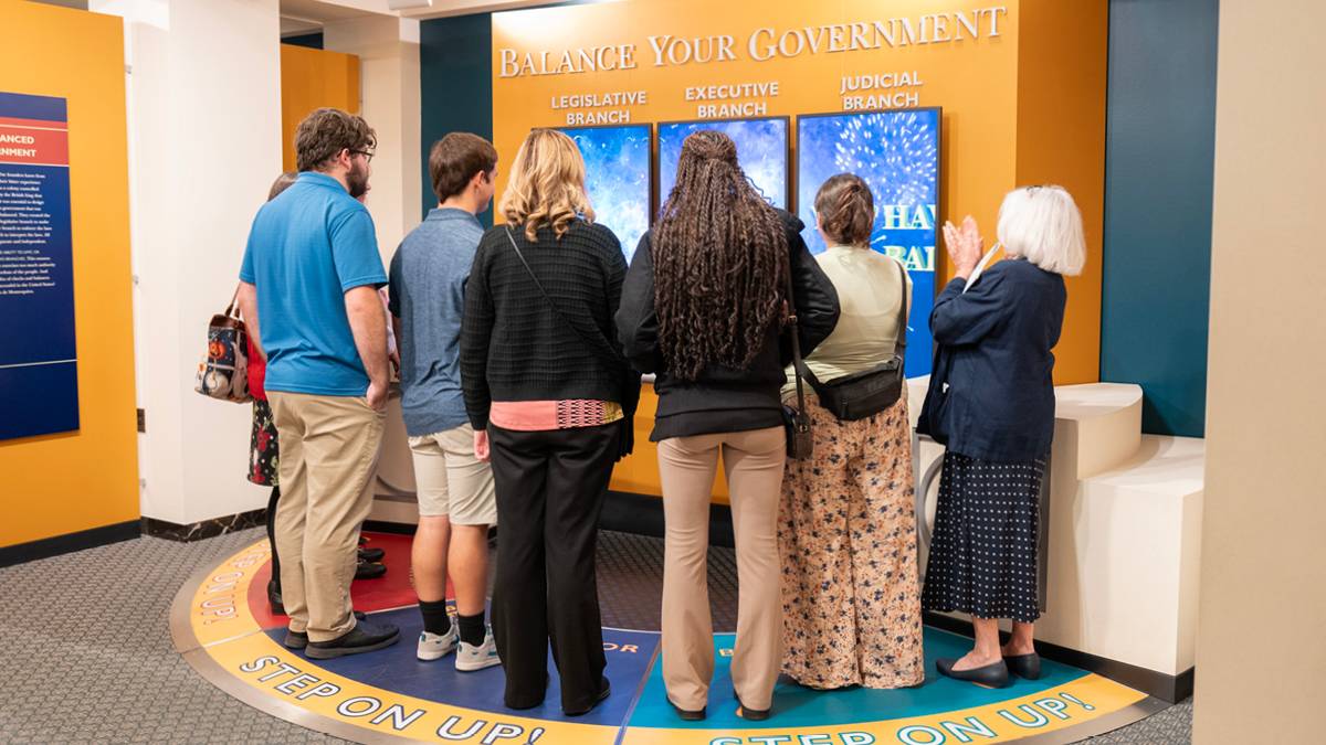 A group of six standing around a three large interactive screens.