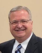 Image of a man wearing a dark suit and blue tie.