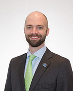 Image of a bald man with a close-shaved beard wearing a brown suit and a green tie.