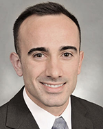 Image of a man with dark hair wearing a brown suit.